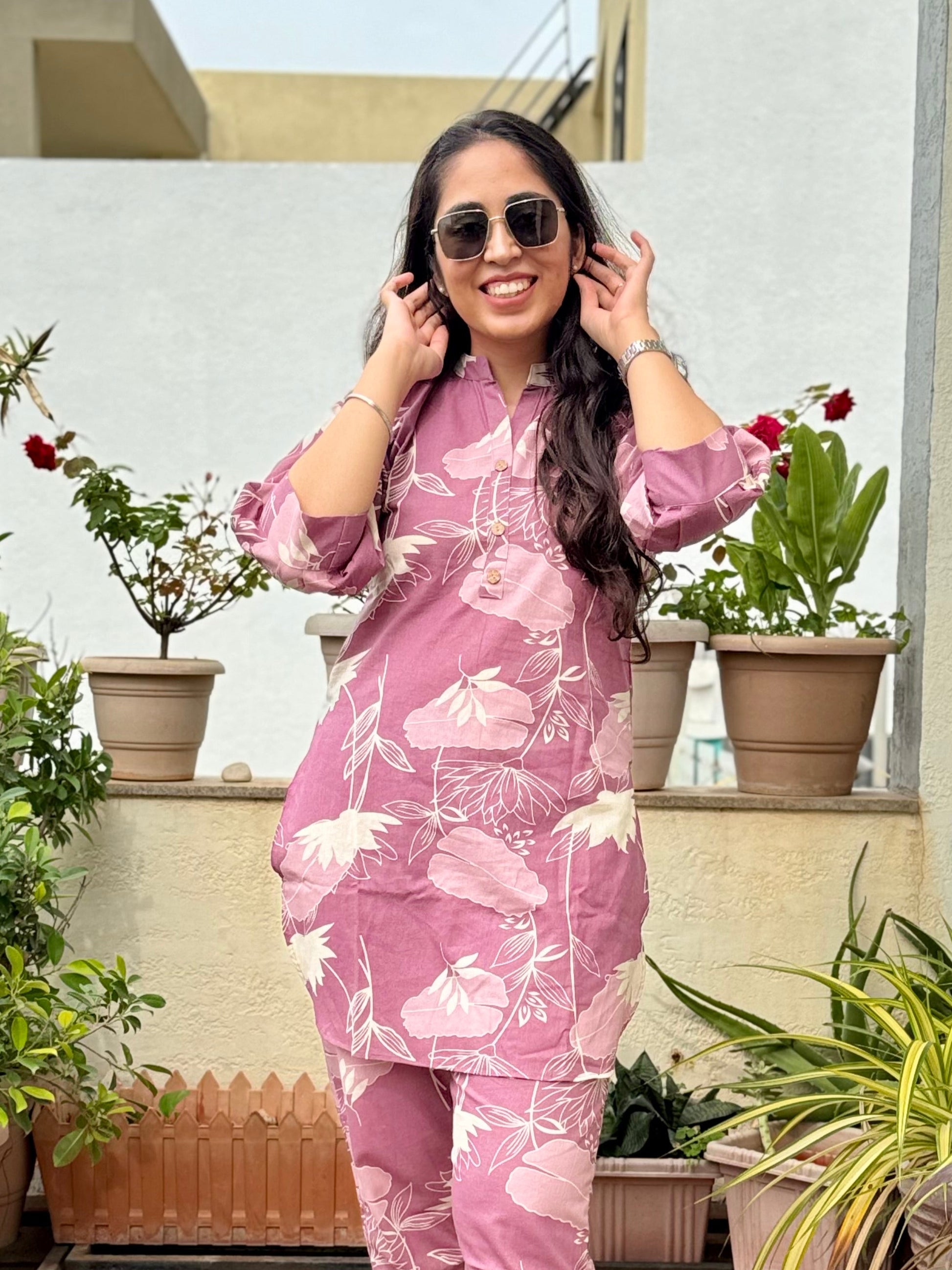 Woman in a pink floral coord set standing on a rooftop with plants around