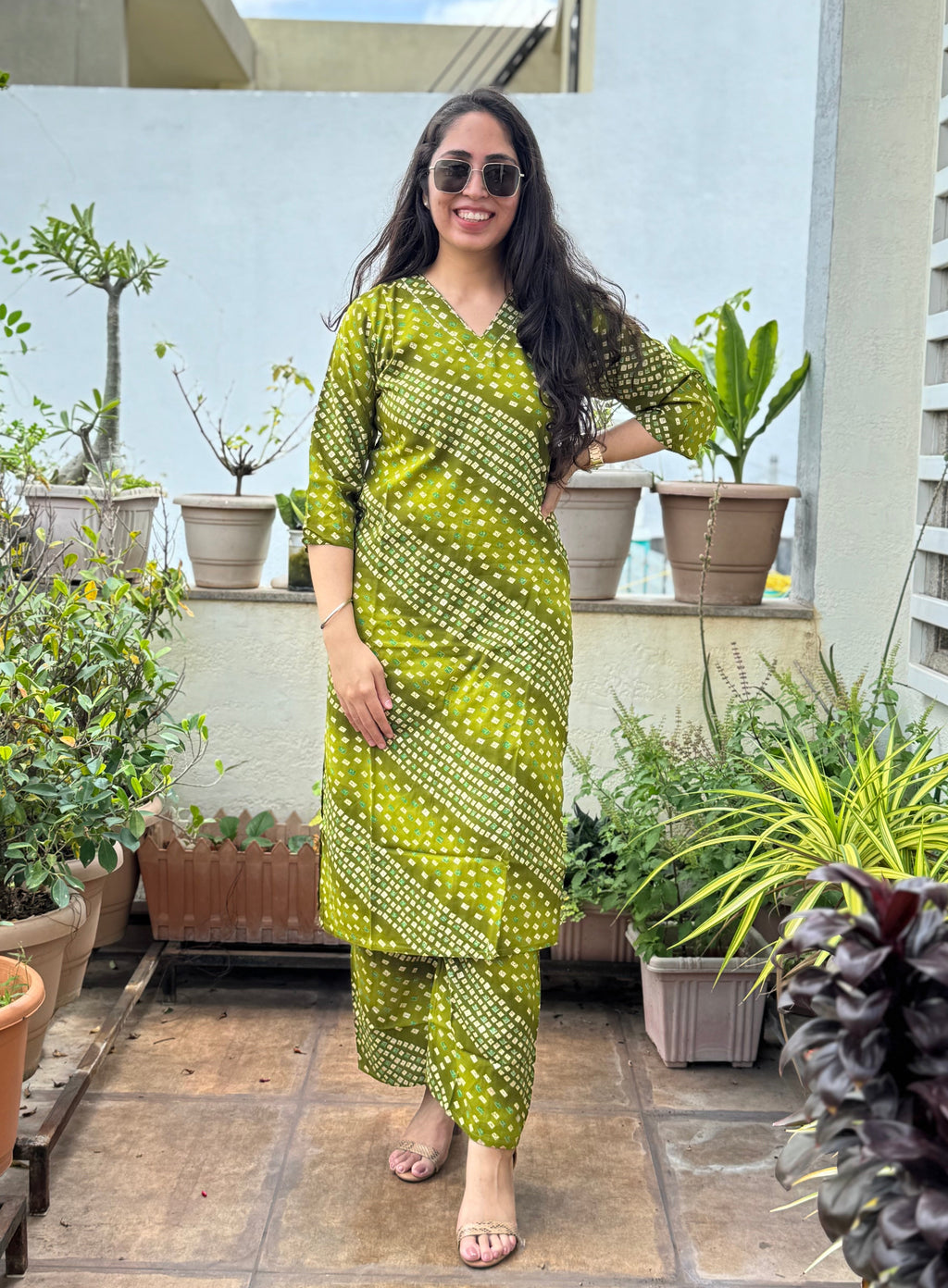 Woman in a green traditional outfit standing on a rooftop terrace with plants.